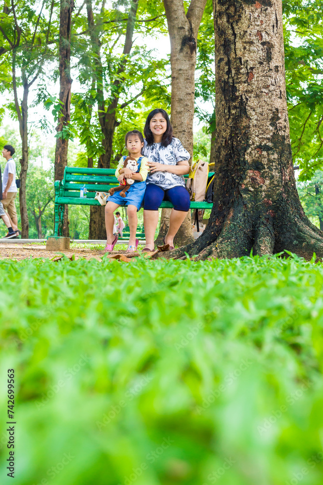 Adorable little asian daughter relax in city publice green park with mom Adorable little asian daughter relax in city publice green park with mom