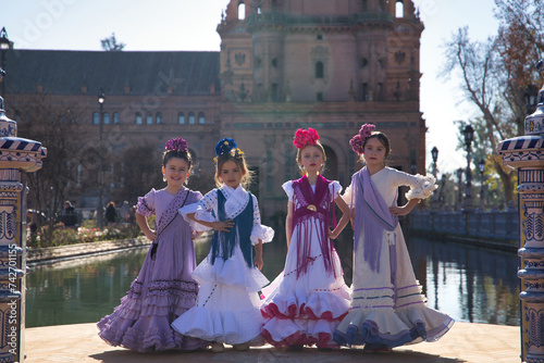 Four girls dancing flamenco, posing looking at the camera, in typical flamenco costumes next to a lake in a beautiful square in Seville. Concept dance, flamenco, typical Spanish, Seville, Spain.