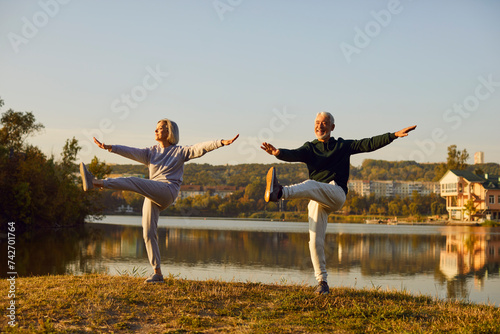 Active sporty senior couple doing stretching exercising in nature. Happy smiling elderly man and woman in sportswear having sport workout in park. Outdoors training and fitness in retirement concept. © Studio Romantic