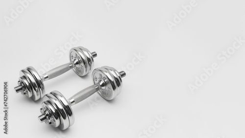 A set of chrome-plated dumbbells, constructed with a steel/iron frame, is shown on a white background, showcasing digital as manual aesthetics in a light silver color.