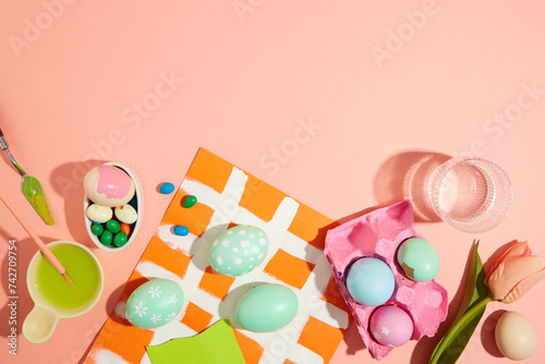 Children's Easter pattern with eggs, concept of holidays. Top view with colorful eggs, chocolate, flower and paintbrush decorated on pink background. Copy space