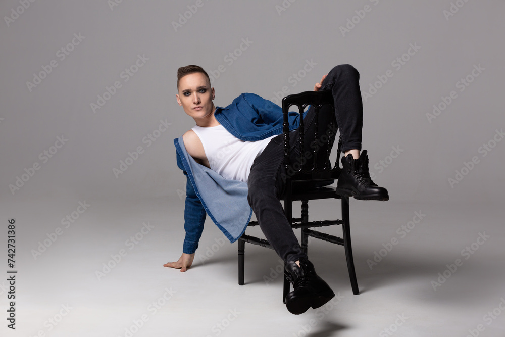 A young man in a blue shirt with rock musician makeup poses on a chair. A young man in a blue shirt with rock musician makeup poses on a chair.