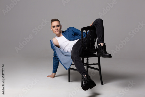 A young man in a blue shirt with rock musician makeup poses on a chair.