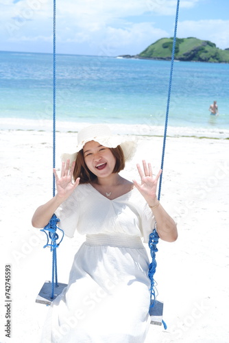 Woman in white dress and hat swinging on tropical beach, sunny day, good weather on lombok beach