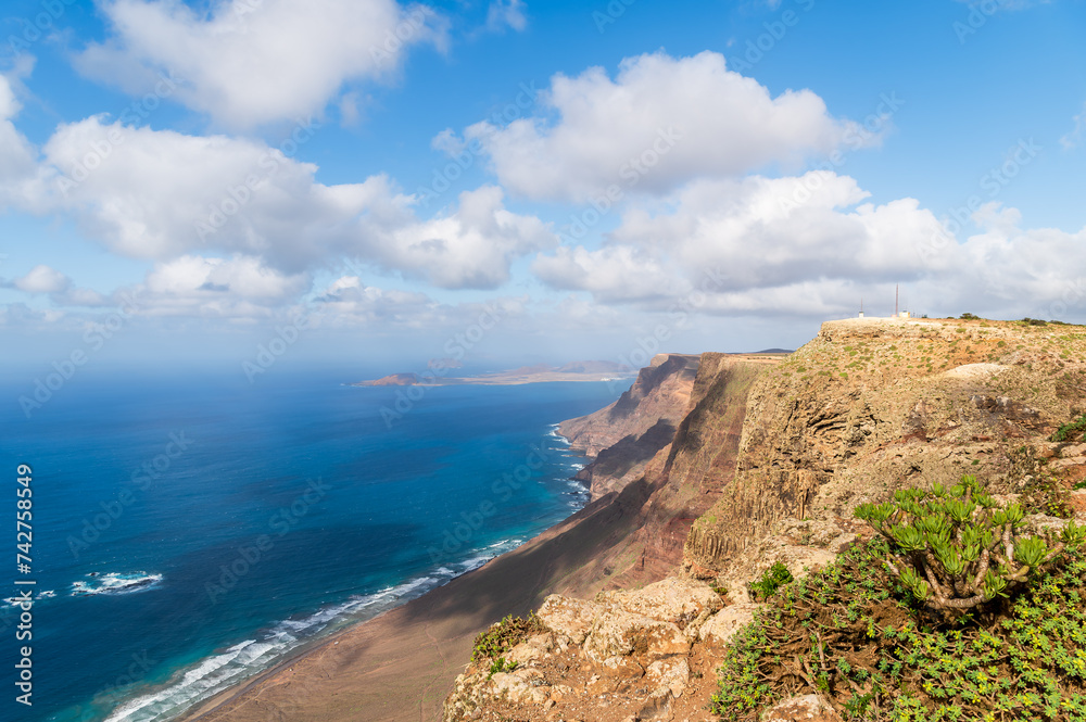 Sweeping views of Playa Famara, Lanzarote, with its golden sands embraced by azure waters and dramatic cliffs, a surfer haven.