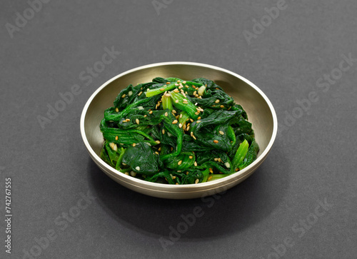 Spinach Salad. A traditional Korean side dish of spinach moochim served in a brass bowl. Boiled spinach seasoned with sesame oil. 