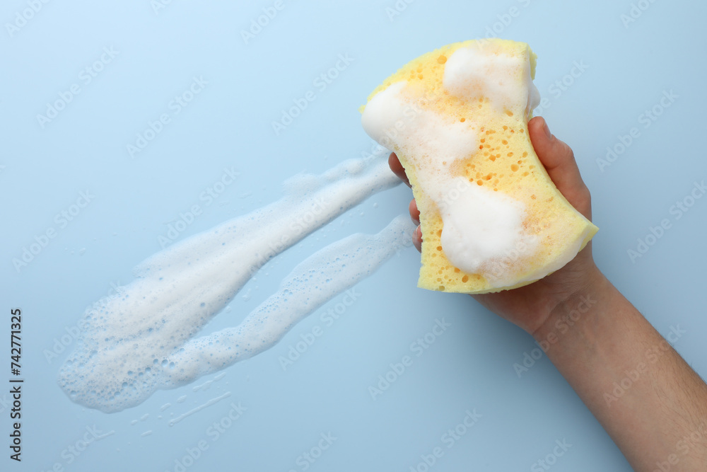 Man holding sponge with foam on light blue background, top view Man holding sponge with foam on light blue background, top view
