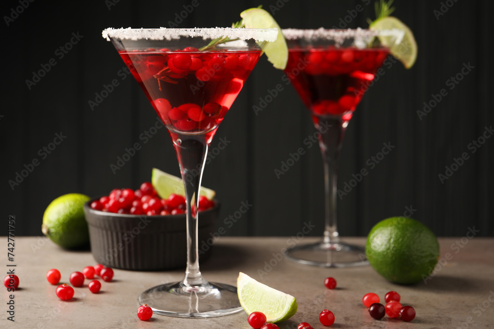 Tasty cranberry cocktail with rosemary and lime in glasses on grey table against black background Tasty cranberry cocktail with rosemary and lime in glasses on grey table against black background