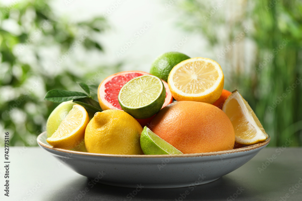Different fresh citrus fruits and leaves on grey table against blurred background, closeup Different fresh citrus fruits and leaves on grey table against blurred background, closeup