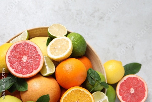 Different fresh citrus fruits and leaves in bowl on light table, flat lay. Space for text © New Africa