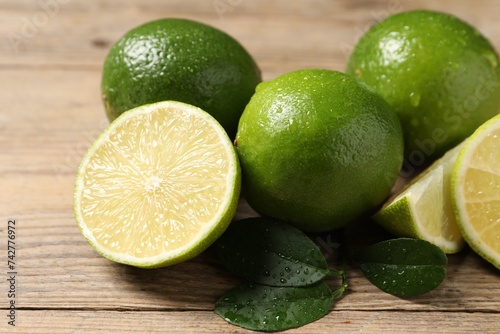 Fresh ripe limes and green leaves with water drops on wooden table, closeup