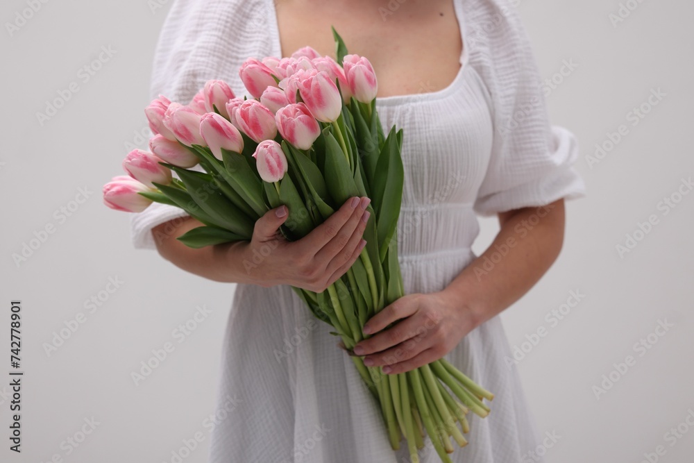 Woman with bouquet of beautiful fresh tulips on light grey background, closeup