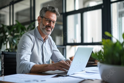 Smiling mature professional business man manager looking at report in office. Happy mid aged businessman company executive working in office with laptop reading financial account, Generative AI