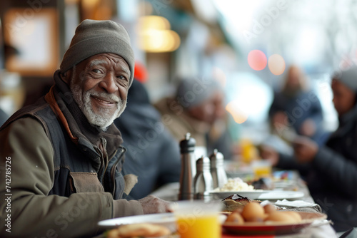 Positive homeless African American man standing at the table in a street dining hall, surrounded by other individuals