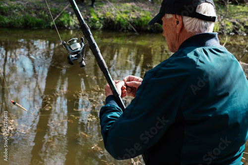 Back view of fisherman in a river. View from behind of a man fishing in the river. He is holding his rod and putting the bait on the hook.