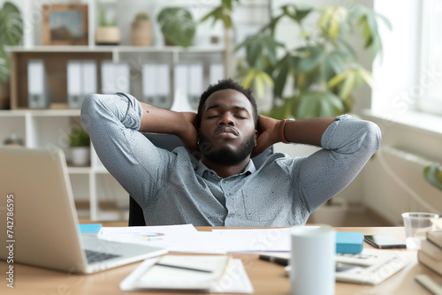 Business bookkeeper financial accountant feels tired but satisfied after completing big work amount. Relaxed young Black man with hands behind head sitting at office desk with laptop computer