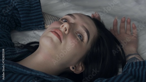 Female in sleepwear laying on the bed in the studio. Young woman in pajama shirt laying posing under thin sheet of oilcloth wrap. photo