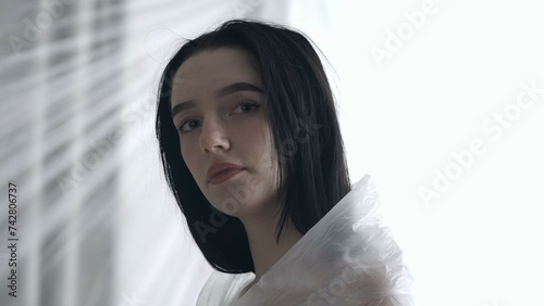 Female in underwear posing in the studio. Young woman in lingerie seminude posing at camera under thin sheet of oilcloth wrap.