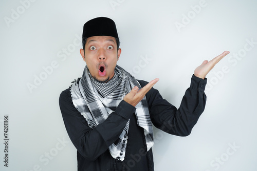 Wow face shocked expression Asian Muslim man wearing Arab turban sorban pointing hand finger at empty space on isolated background photo