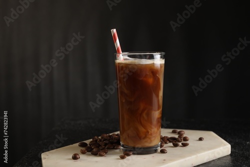 Refreshing iced coffee with milk in glass and beans on table against dark gray background, space for text