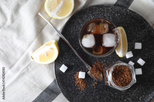 Refreshing iced coffee in glass, sugar cubes, lemon and spoon on cloth, top view