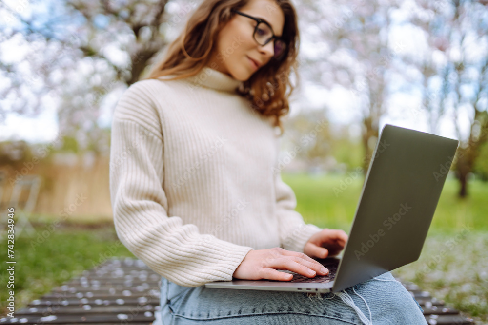 Young woman working outdoors enjoying the good weather in the blooming park. Freelance, technology, education, business, blogging concept.