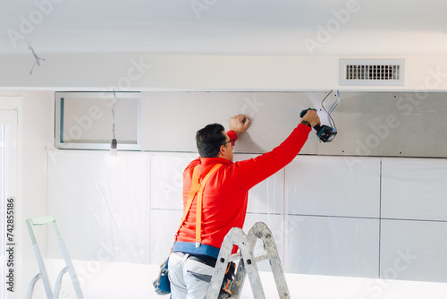 Plasterboard worker installs a plasterboard wall on the kitchen cabinets to cover the extractor pipe of the hood. photo
