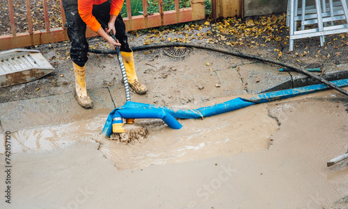 A worker repairs a broken water pipe on the street by using a pump to empty the trench.