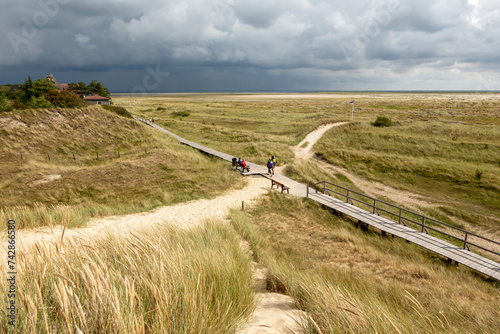 People walk on boardwalk at Kniepsand beach, Wittdun, Amrum island, North Frisia, Germany photo