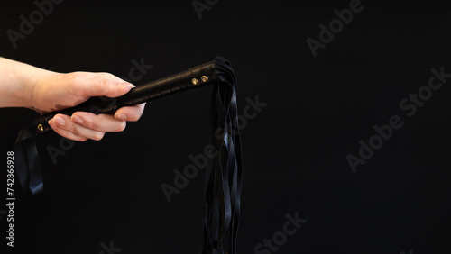 A woman's hand holds a whip against a dark background. Leather whip for spanking isolated on black. Sex toy for intimacy. Sexual slavery