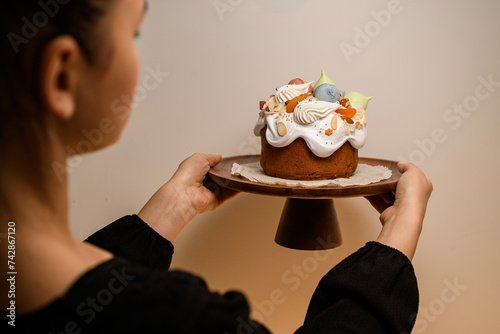 Baker in a black dress turns his back to the camera and holds a beautifully decorated Easter cake on a stand