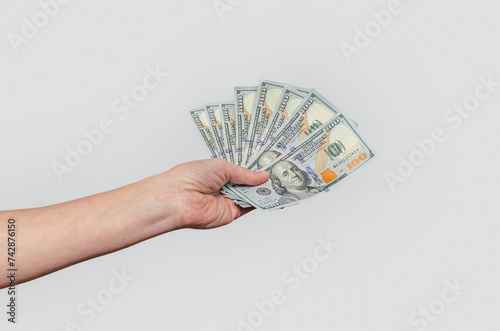 Female hand with fan of dollar banknotes, gray background. Concept of payments, financial stability.