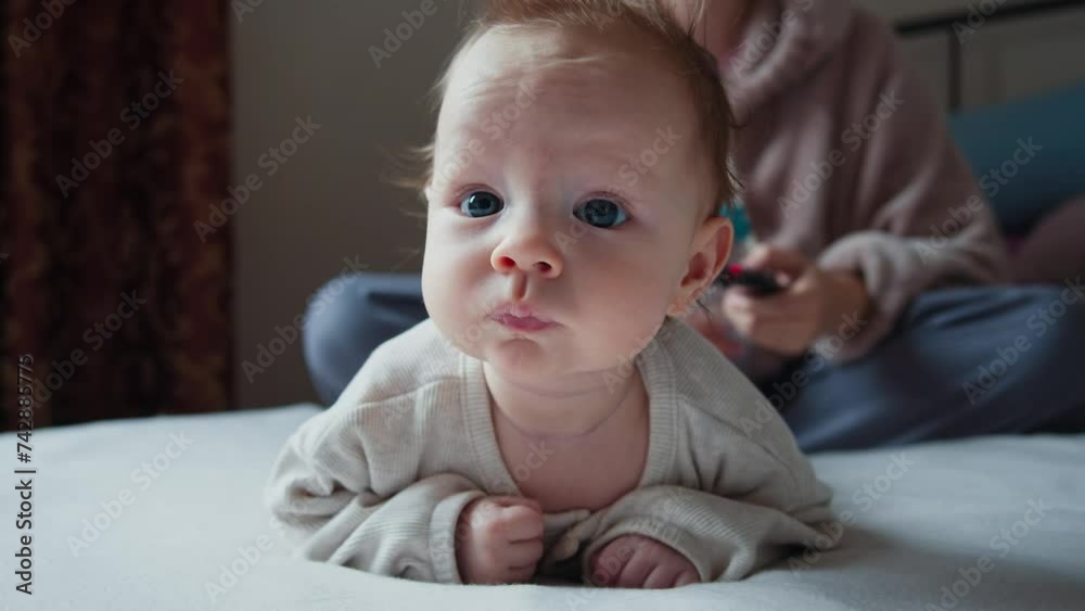 A contemplative baby with wide blue eyes lies on a bed, gazing thoughtfully. The soft, neutral tones of the room and the infant's clothing convey a serene atmosphere. A contemplative baby with wide blue eyes lies on a bed, gazing thoughtfully. The soft, neutral tones of the room and the infant's clothing convey a serene atmosphere.