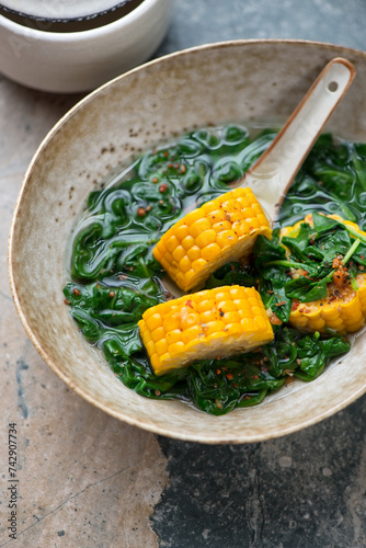 Bowl of sayur bening or clear spinach and corn soup, vertical shot on a grey and beige granite background, middle closeup