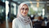 Close-up portrait of Muslim businesswoman in hijab smiling and looking at camera, female worker in glasses working inside modern office building