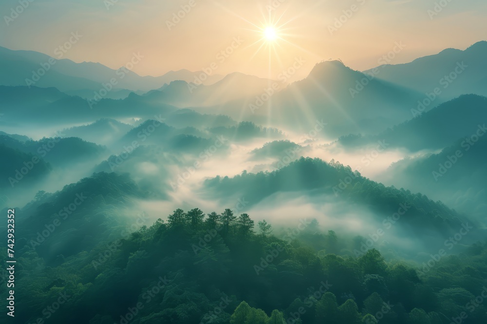 Aerial view of mountains covered in fog with sun rising behind a fog covered forest - obrazy, fototapety, plakaty 