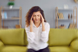Woman feels dizzy and sits down on the couch. Young woman sitting on the sofa at home, feeling pain and a spinning sensation in her head. Concept of headache, vertigo, health problem, brain tumor