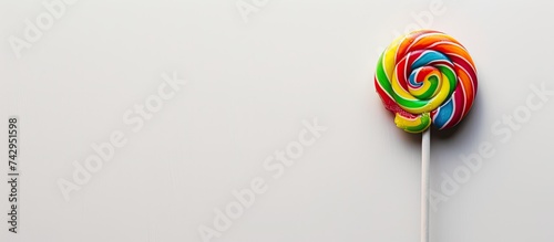 A bright and colorful lollipop on a stick stands out against a clean white background. The lollipop features a retro design, with a variety of vibrant colors swirling together. photo