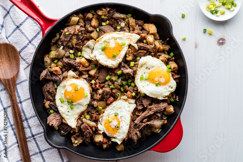 A pan filled with roast beef hash topped with fried eggs, ready for serving.