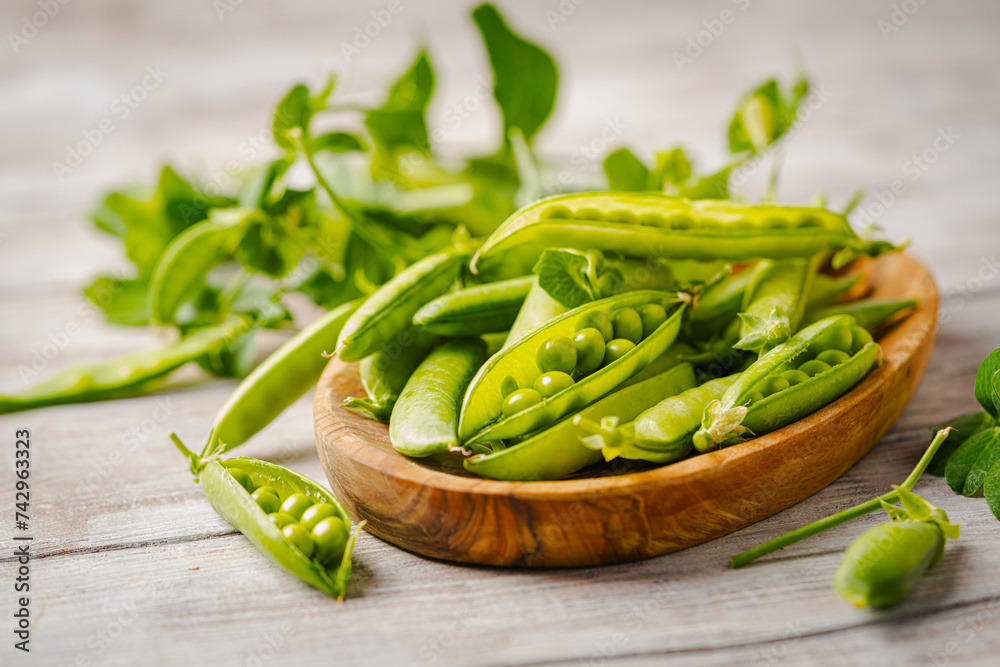 Fresh green peas in wooden bowl with pods and leaves on white wooden table, healthy green vegetable or legume Fresh green peas in wooden bowl with pods and leaves on white wooden table, healthy green vegetable or legume