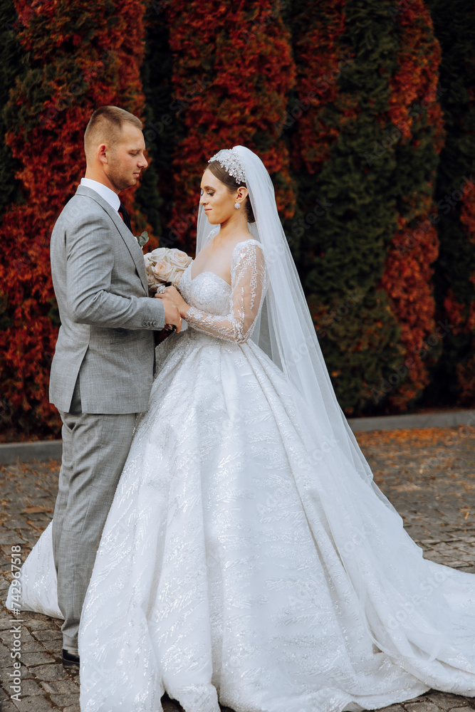 Fototapeta premium Wedding couple on a walk in the autumn park. The bride in a beautiful white dress. Love and relationship concept. Groom and bride in nature outdoors