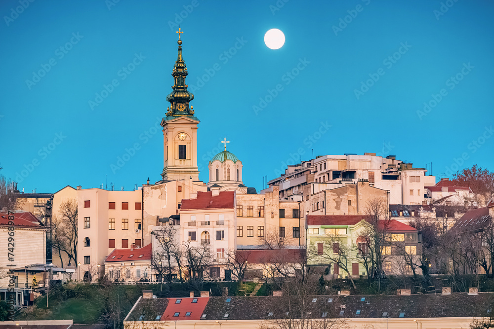 Discover Belgrade's architectural beauty, with churches and towers overlooking the scenic Danube River at night with fullmoon