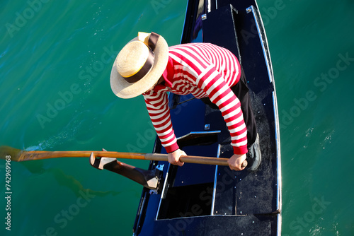 Venetian gondolier with hat rowing on gondola on grand canal in Venice in Italy