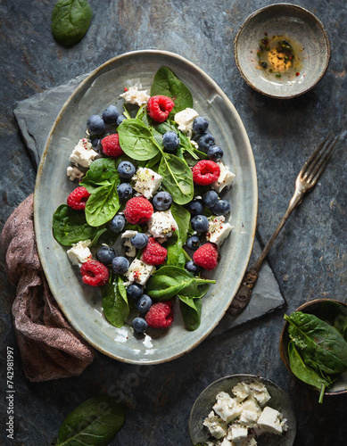 Bunter Salat mit frischen Beeren zartem Spinat und cremigem Fetakäse Ein leichtes und gesundes Geschmackserlebnis auf Holzbrett photo