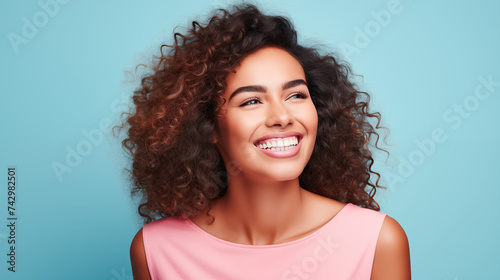 Curly girl with dark hair and perfect skin smiling and showing her white teeth on a blue background  banner with space for your text