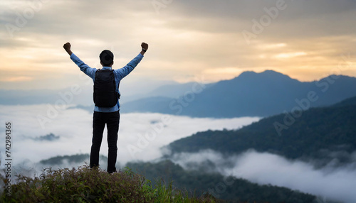 Silhouette of person with raised hand at mountain peak in foggy sunrise, symbolizing success