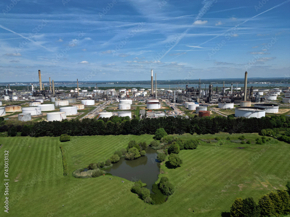 Green belt with fishing pond and public access to it in front of the biggest oil refinery and petrochemical complex in the UK based in Fawley, Southampton. Panoramic aerial view on fuel storage tanks.