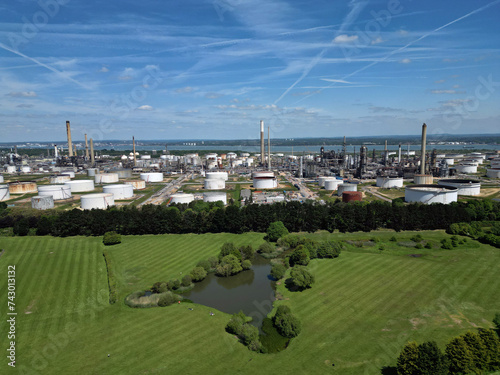 Obraz na płótnie Green belt with fishing pond and public access to it in front of the biggest oil refinery and petrochemical complex in the UK based in Fawley, Southampton. Panoramic aerial view on fuel storage tanks. w salonie