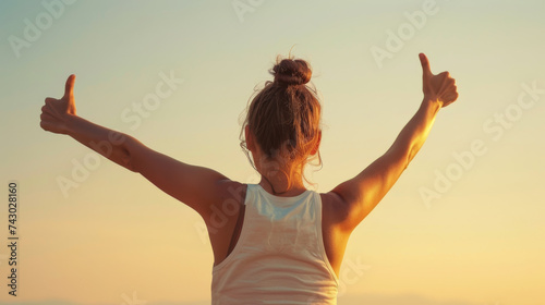 a person from behind, raising their arms with thumbs up towards the sky as the sun sets or rises, embodying a sense of accomplishment and positivity.