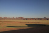 red desert sand plaine with bright green fresh grass growing, red mountain range in the background